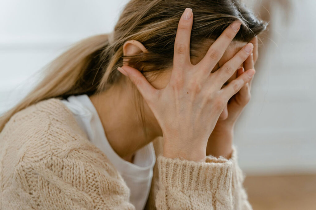 A person with long hair and a beige jumper sits with their head in their hands, covering their face—an image reflecting the distress often caused by intrusive thoughts and OCD.